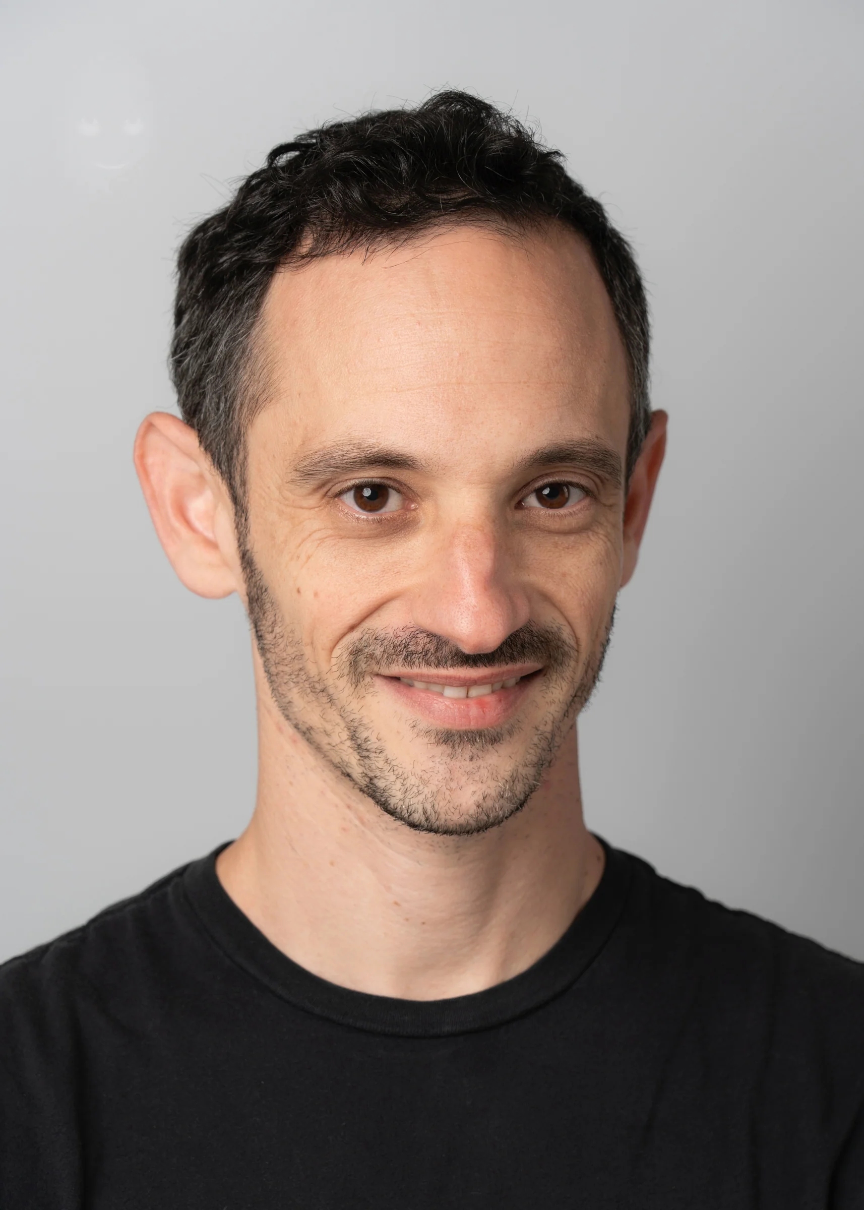 Portrait of a man with brown hair and glasses on a flat gray background.