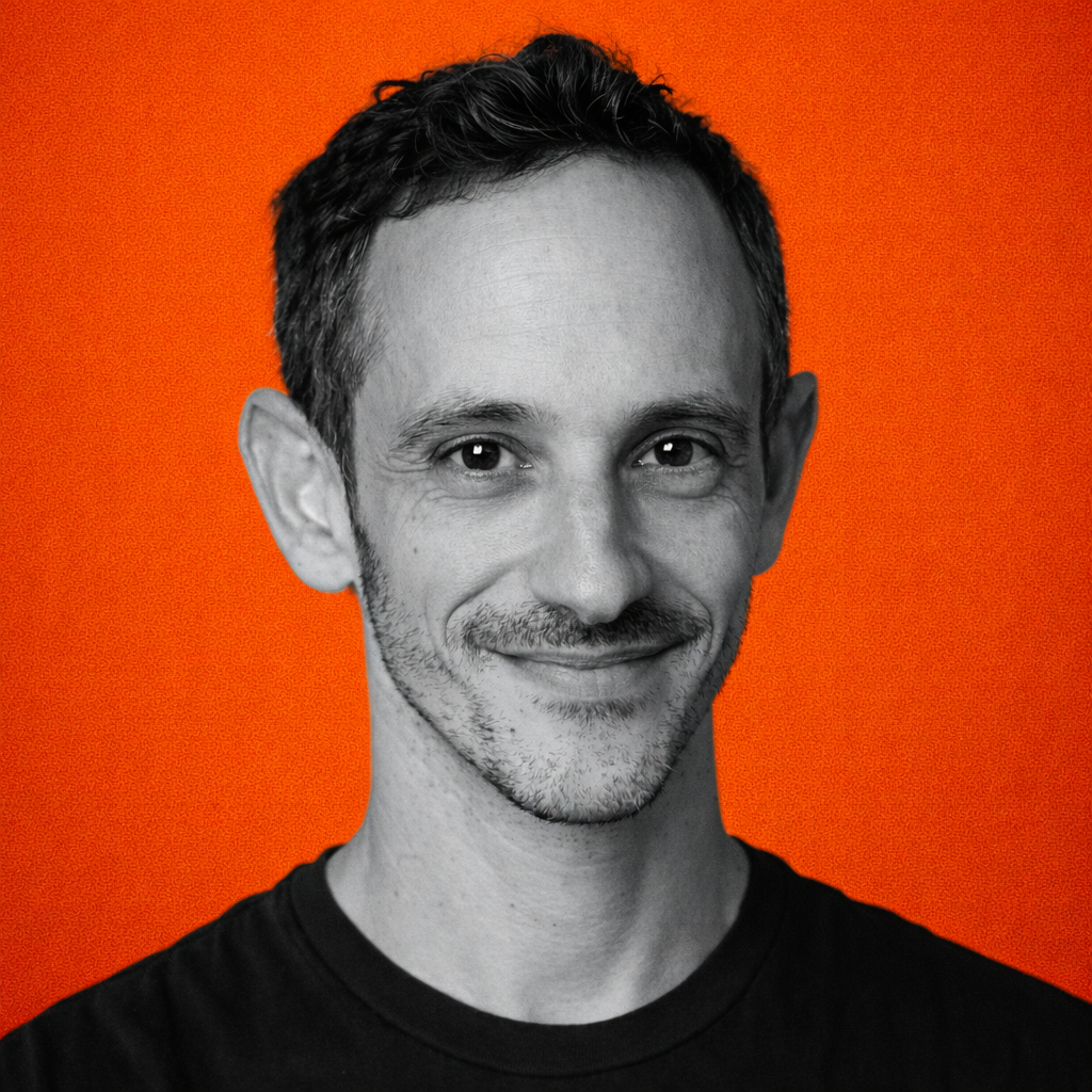 Portrait of a man with brown hair and glasses on a flat gray background.
